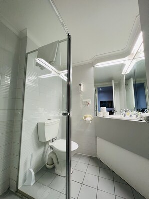 Bathroom features a glass-enclosed shower, toilet, sink, and towel rack.