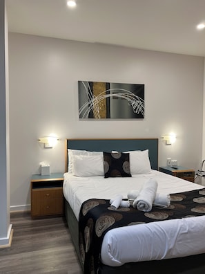 Relax in a serene space with a neatly made bed, a wooden nightstand, and a wall-mounted artwork.
