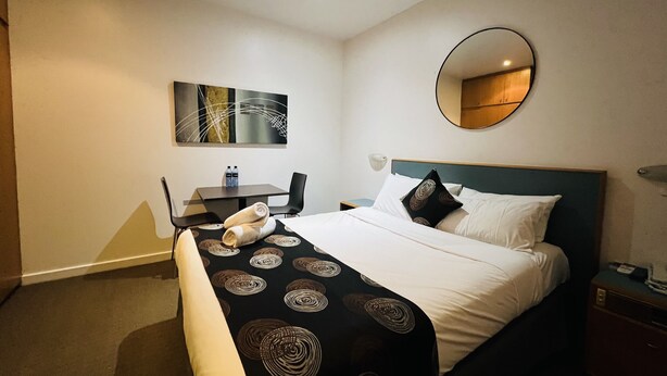 Ein Hotelzimmer mit Bett, Schreibtisch, Stuhl, rundem Spiegel und einem Wandbild.