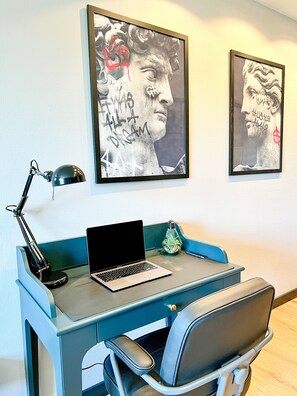 A desk with a laptop, a desk lamp, and a chair. There are two framed artworks on the wall. - JUPAS° Loft34 – Studio, Carport & Workspace (Trier)