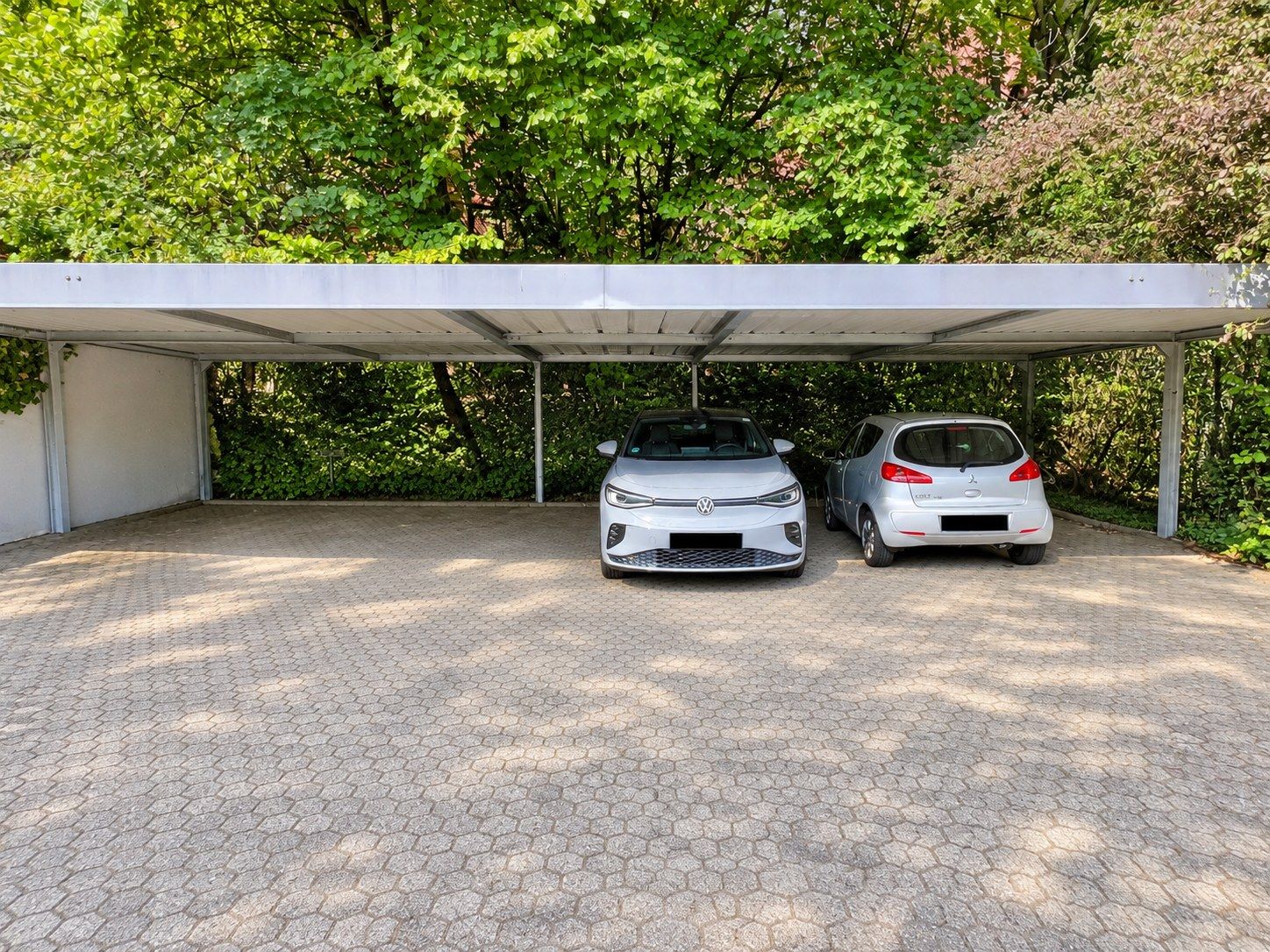 Un'area di parcheggio coperta con due auto parcheggiate, immersa nel verde.