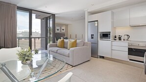 A modern apartment with a living area featuring a glass table, a sofa with cushions, and a view of the city through large windows. - Cosmopolitan 401 (Cape Town)