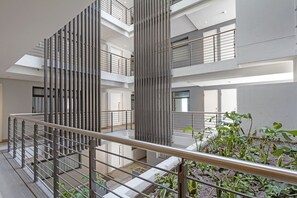 En interiör med flera nivåer, ett centralt atrium, metallräcken och inomhusväxter.