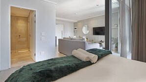 A modern hotel room with a large bed, a green furry rug, a grey sofa, a bathroom with a shower, and a large window with curtains. - Cosmopolitan 401 (Cape Town)