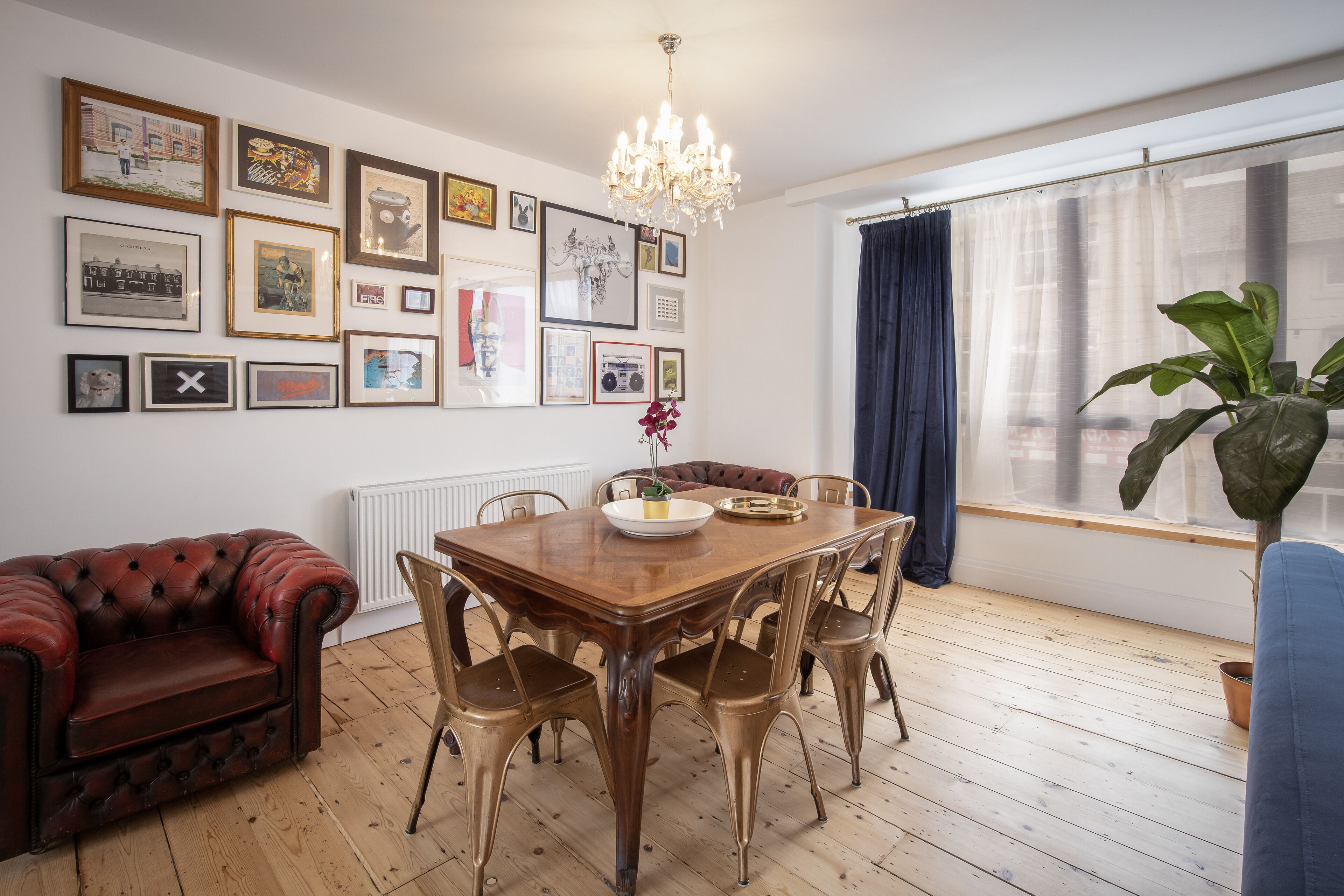 A dining area with a wooden table, metal chairs, a chandelier, and a large window with curtains.