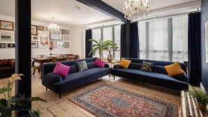 A modern living room with a dark blue sectional sofa, a patterned rug, and a chandelier. - Blueberries Apartments by Sasco (Blackpool)