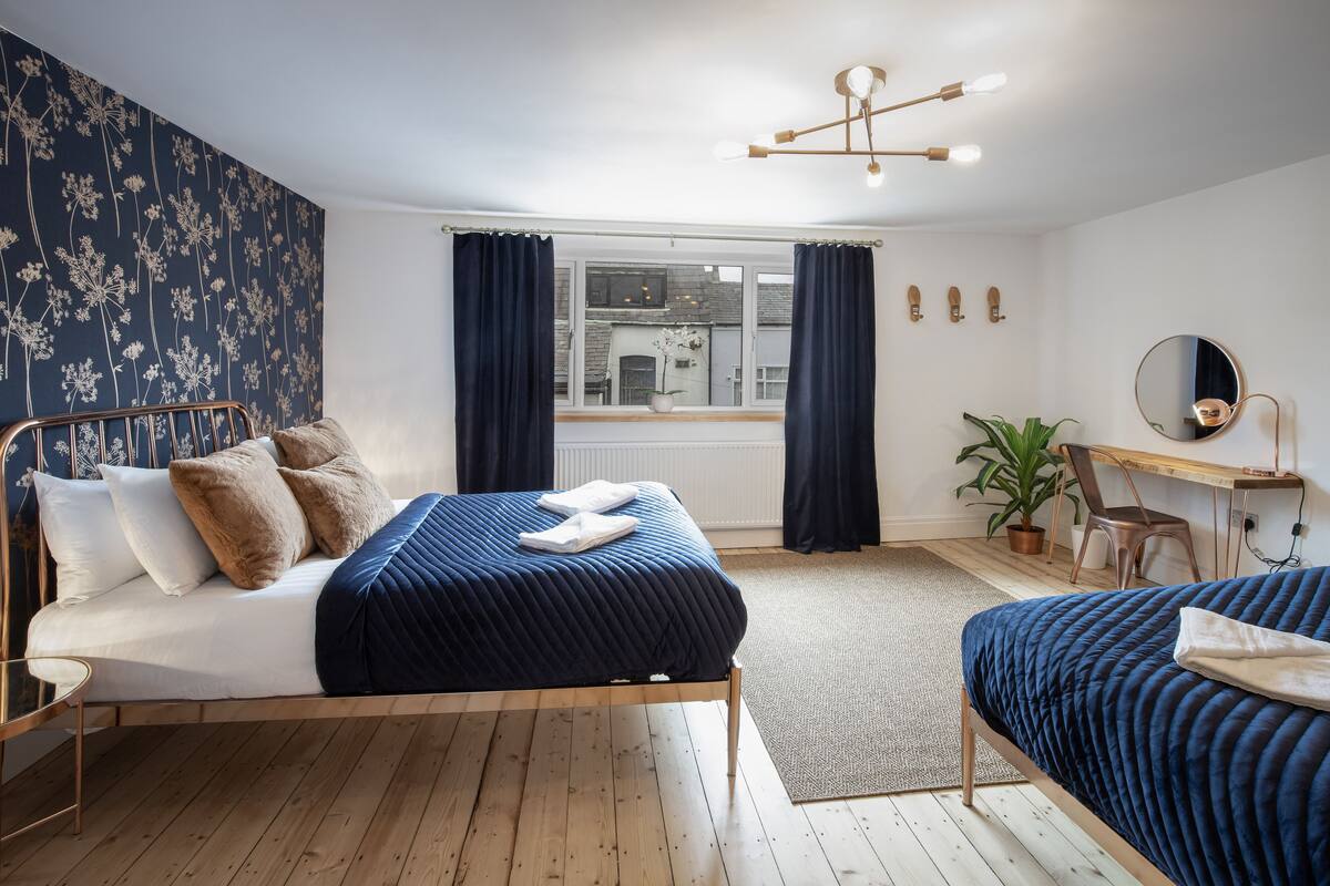 A bedroom with a bed, a desk, a chair, a potted plant, and a view of the outside.