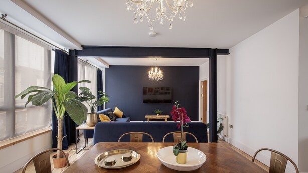 A dining area with a wooden table, chairs, a chandelier, and a potted plant. - Blueberries Apartments by Sasco (Blackpool)