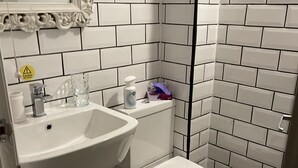 Un baño con azulejos blancos, un lavamanos, un inodoro y un espejo.