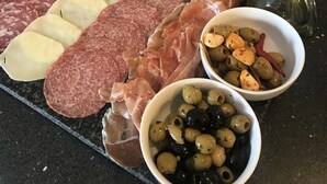 Una tabla de fiambres con diversos embutidos, quesos y aceitunas sobre una encimera negra.