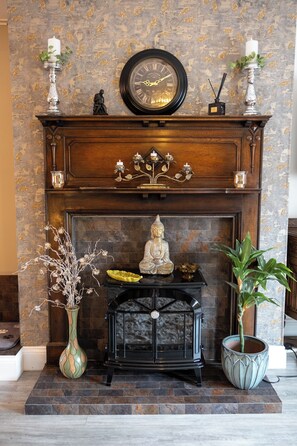 A fireplace with a clock above it, a Buddha statue, and two potted plants.