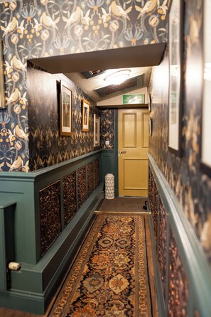 A hallway with patterned wallpaper, framed pictures, a door, and a patterned carpet. - The Old Clock Tower Central Skipton Luxury Apartment 60+ 5* Reviews on platforms (Skipton)