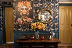 A room with a decorative mirror, a floral painting, and a vase with flowers on a wooden table. - The Old Clock Tower Central Skipton Luxury Apartment 60+ 5* Reviews on platforms (Skipton)