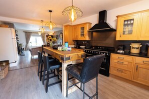 A modern kitchen with wooden cabinets, a central island with bar stools, and a black stove. - The Old Clock Tower Central Skipton Luxury Apartment 60+ 5* Reviews on platforms (Skipton)