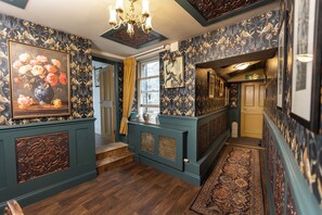 A hallway with patterned wallpaper, a chandelier, and a wooden floor.