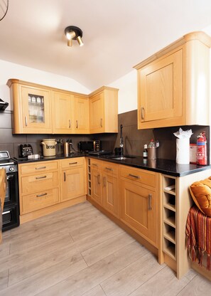 A modern kitchen with wooden cabinets, a black countertop, and a built-in oven. - The Old Clock Tower Central Skipton Luxury Apartment 60+ 5* Reviews on platforms (Skipton)
