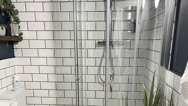 Un baño moderno con ducha envuelta en vidrio, paredes de azulejos blancos, un inodoro y un lavabo.