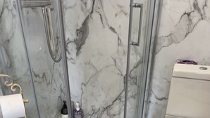 Un baño con cabina de ducha de vidrio, inodoro y suelo a cuadros.