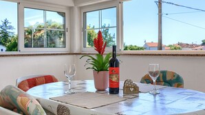 Une table ronde recouverte d’une nappe blanche, deux verres à vin, une bouteille de vin, une plante en pot et une boîte décorative.