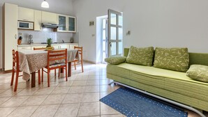 Un espace de vie compact comprenant une kitchenette, un coin repas et un canapé vert.