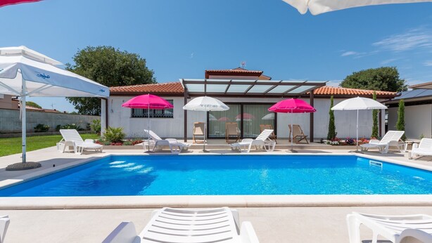 A swimming pool with white lounge chairs and umbrellas, a modern building with a tiled roof, and a clear blue sky. - Apartment Nino by Interhome (Poreč)