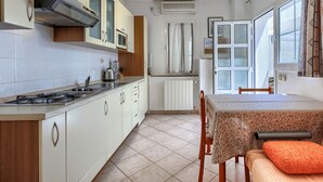 A compact kitchen with white cabinets, a gas stove, and a dining area with a table and chairs. - Apartment Nino by Interhome (Poreč)