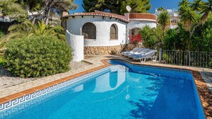 Eine Villa im mediterranen Stil mit Swimmingpool, umgeben von üppiger Vegetation und Palmen.