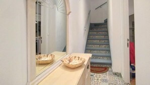 A hallway with a mirror, a wooden vanity, and a staircase with patterned tiles. - Rainbow by Interhome (Benidorm)