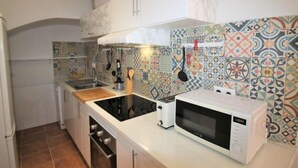 A compact kitchen with a microwave, toaster, and oven. The backsplash features colorful tiles, and there is a hanging rack with utensils. - Rainbow by Interhome (Benidorm)