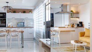 A modern kitchen with white cabinetry, a built-in oven, and a dining area with white chairs and a small table. - Terrasses du Levant by Interhome (Canet-Plage)