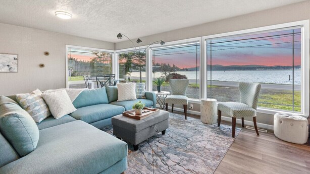 A modern living room with a large window offering a view of a body of water and distant hills. - Waterviews, Gameroom, close to DT, & Ferries! (Port Orchard)