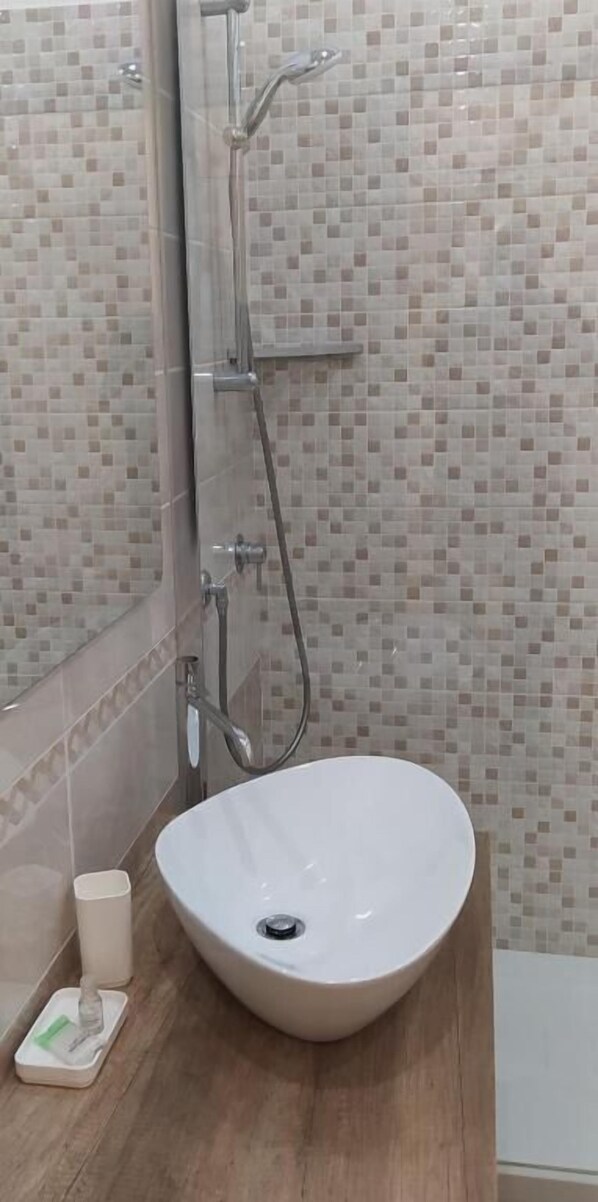 Uma casa de banho com uma pia branca, um chuveiro manual e uma parede revestida a azulejos.