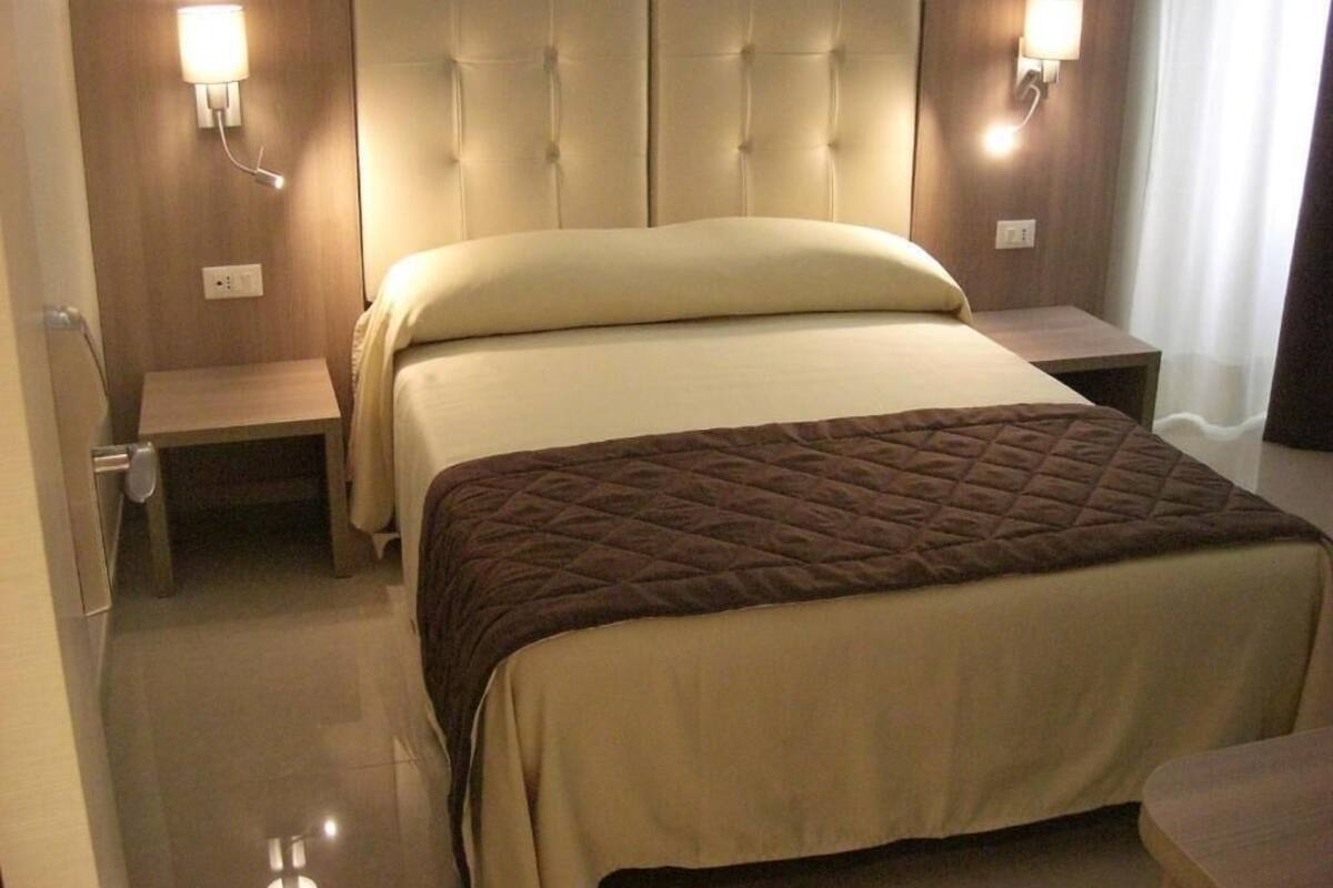 A hotel room with a large bed, two bedside tables, and wall-mounted lamps.