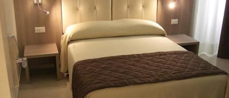 A hotel room with a large bed, two bedside tables, and wall-mounted lamps.
