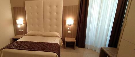 A hotel room with a large bed, two bedside tables, a headboard, and two wall-mounted lamps.