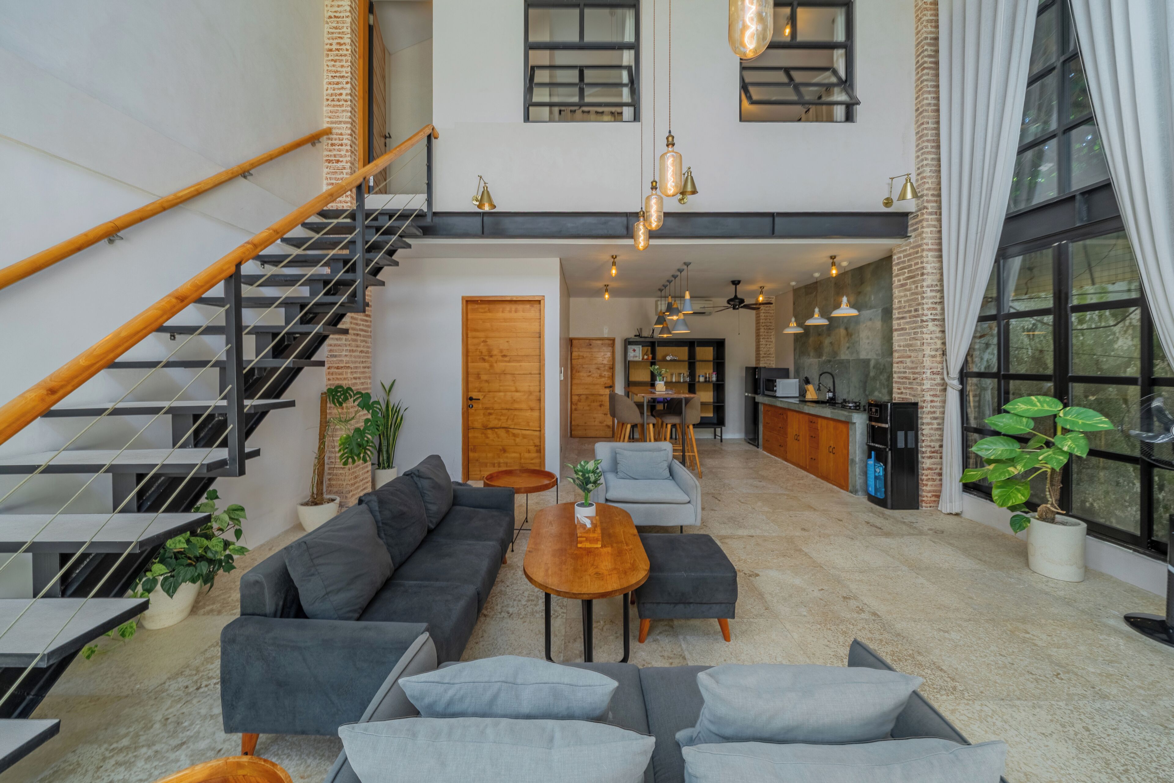 Un intérieur moderne avec un escalier, un coin salon, une cuisine et de grandes fenêtres.