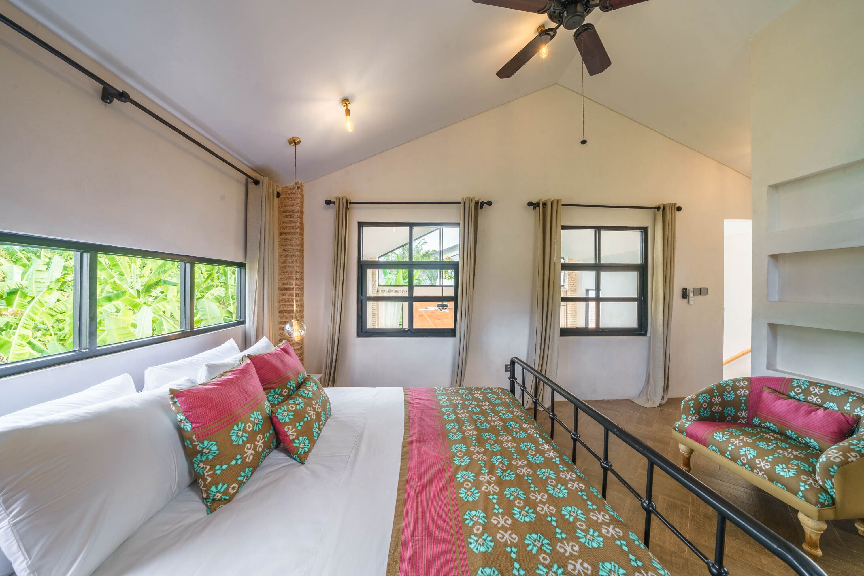 A bedroom with a bed, a sofa, a ceiling fan, and windows with curtains.