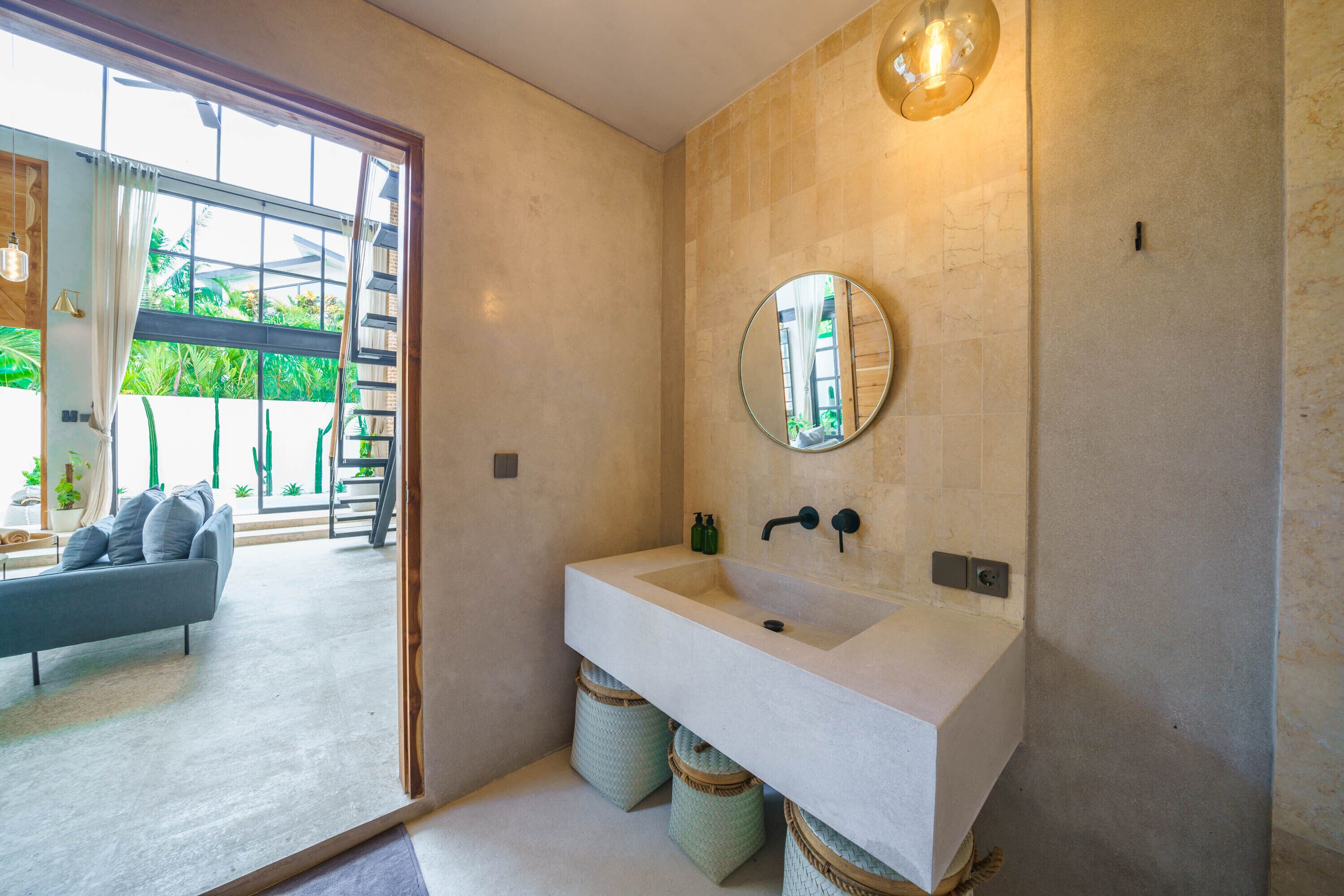 Une salle de bain moderne avec un grand lavabo, un miroir rond et une vue sur un balcon agrémenté de plantes.
