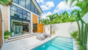 A modern house with a swimming pool, glass doors, and a wooden deck. - Villa Upeksha (Canggu)