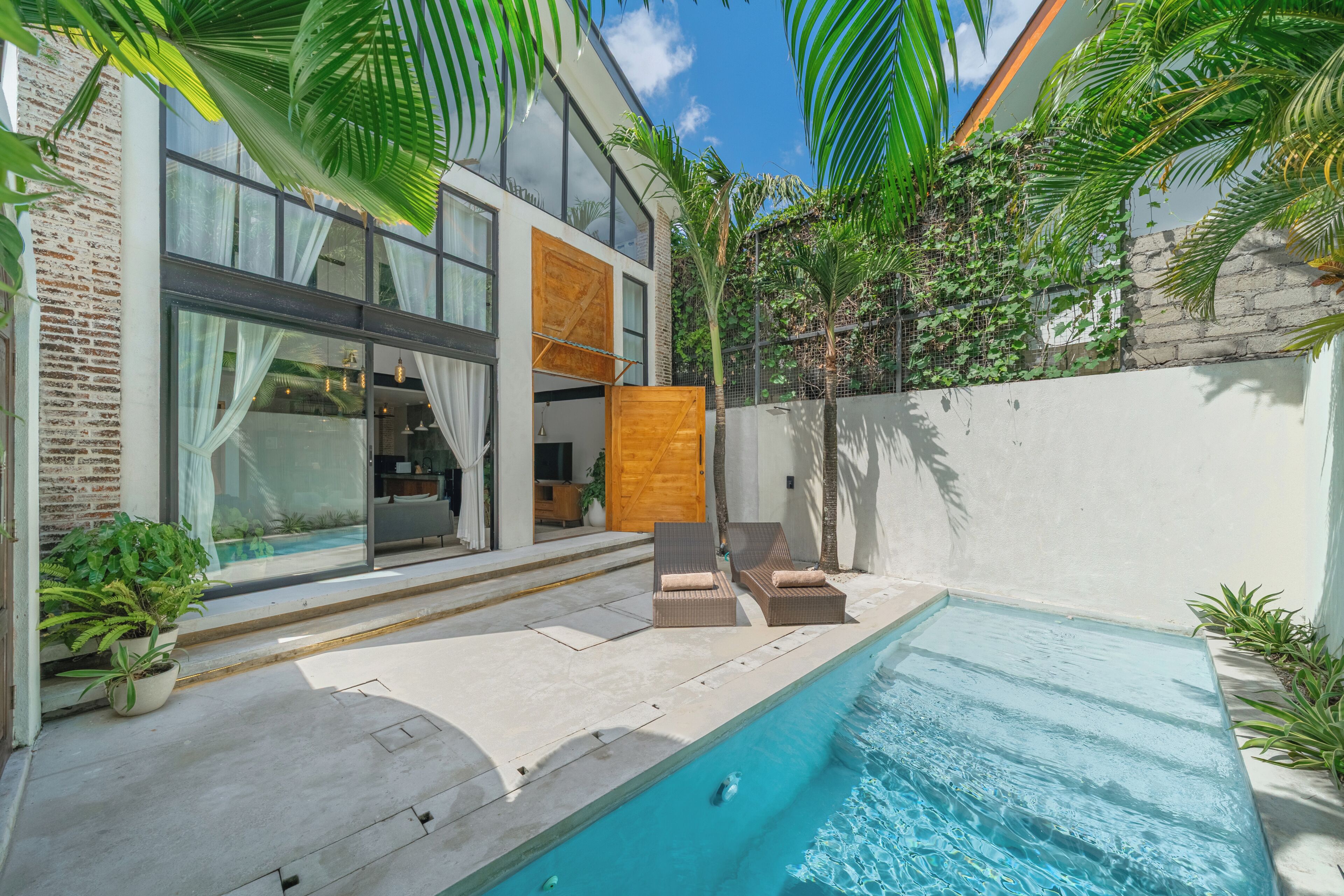 A modern house with a swimming pool, a wooden door, and a balcony with chairs.