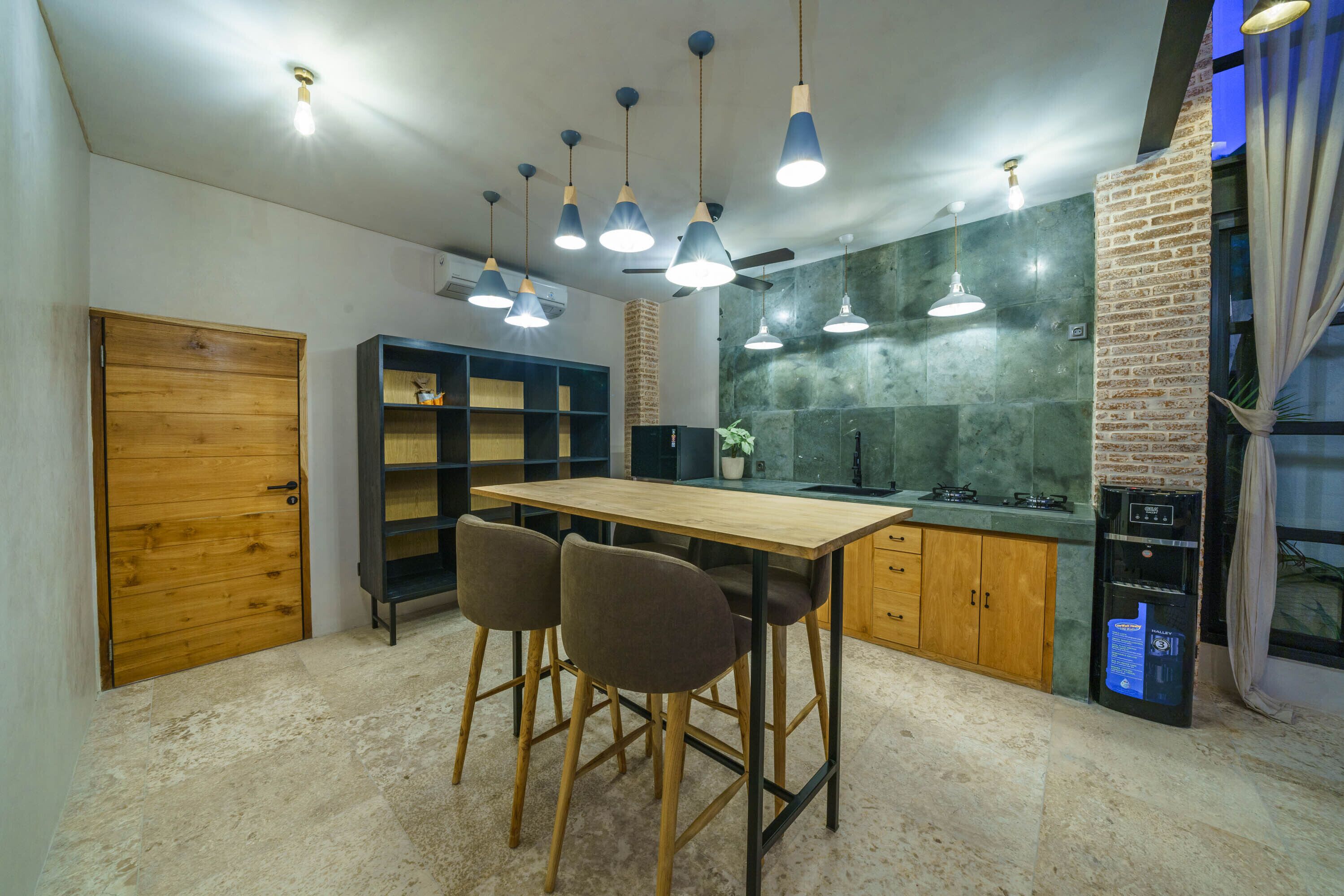 Una cocina moderna con una mesa de madera y taburetes altos, una pared decorativa de ladrillo e iluminación colgante.