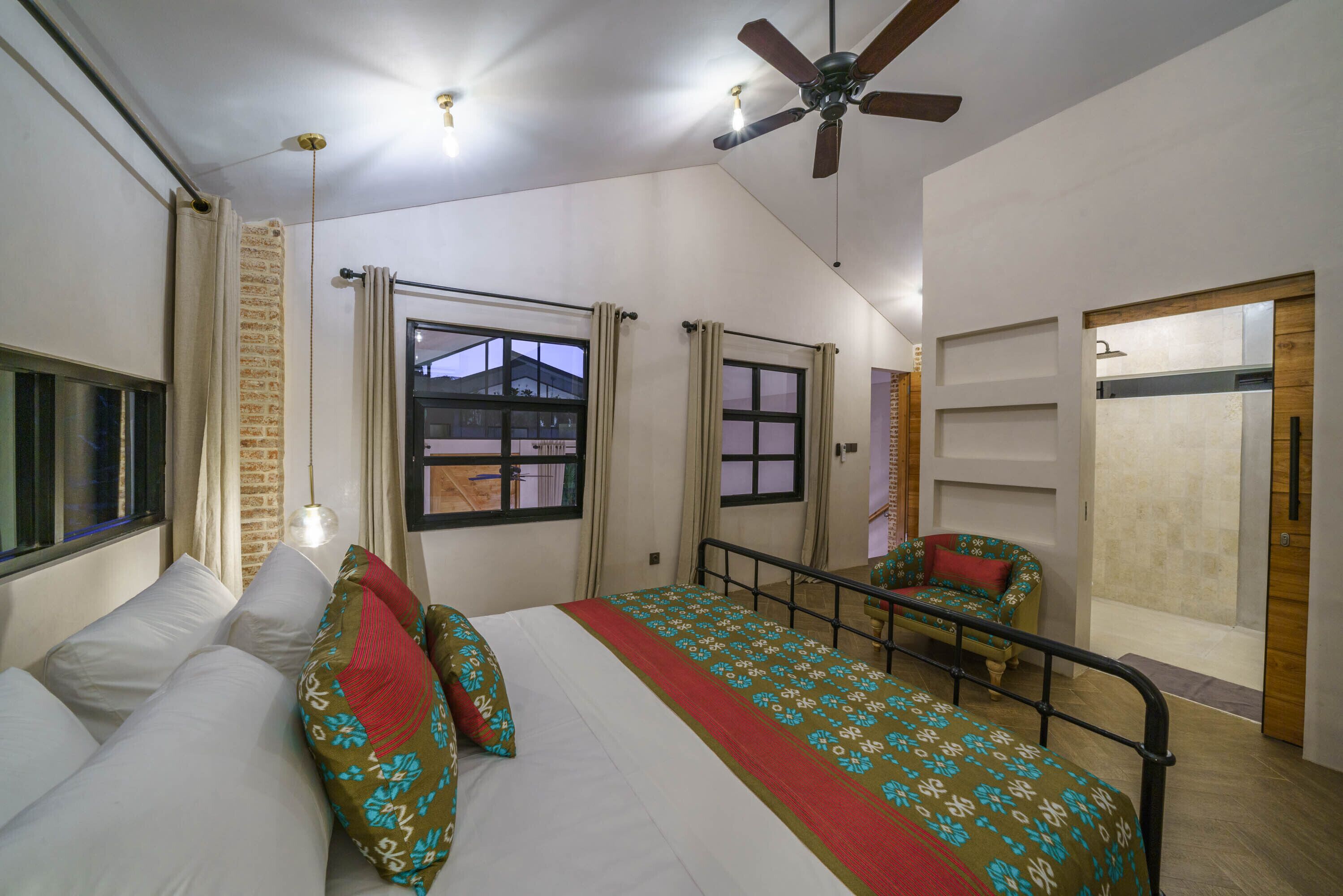 A bedroom with a bed, a chair, a ceiling fan, and a window.