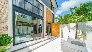 A modern house with large glass windows, a wooden gate, and a patio with outdoor furniture. - Villa Upeksha (Canggu)