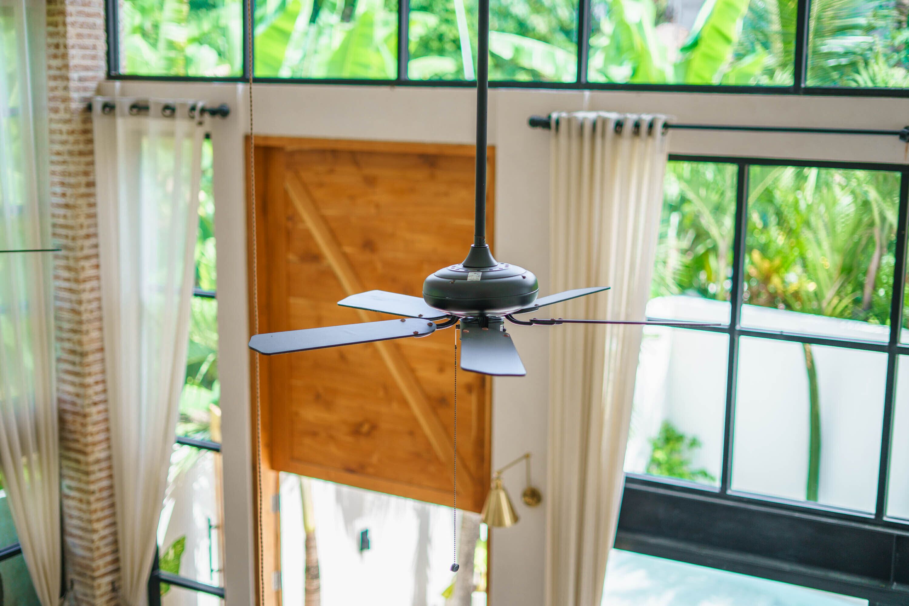 A ceiling fan in a room with large windows and curtains.