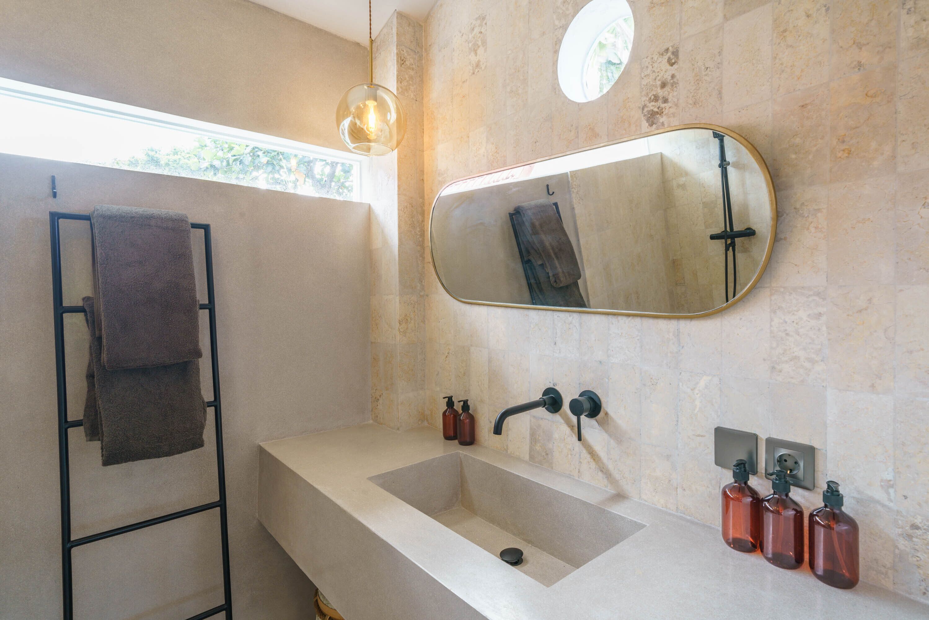 A bathroom with a large sink, a towel rack, a mirror, and two soap dispensers.