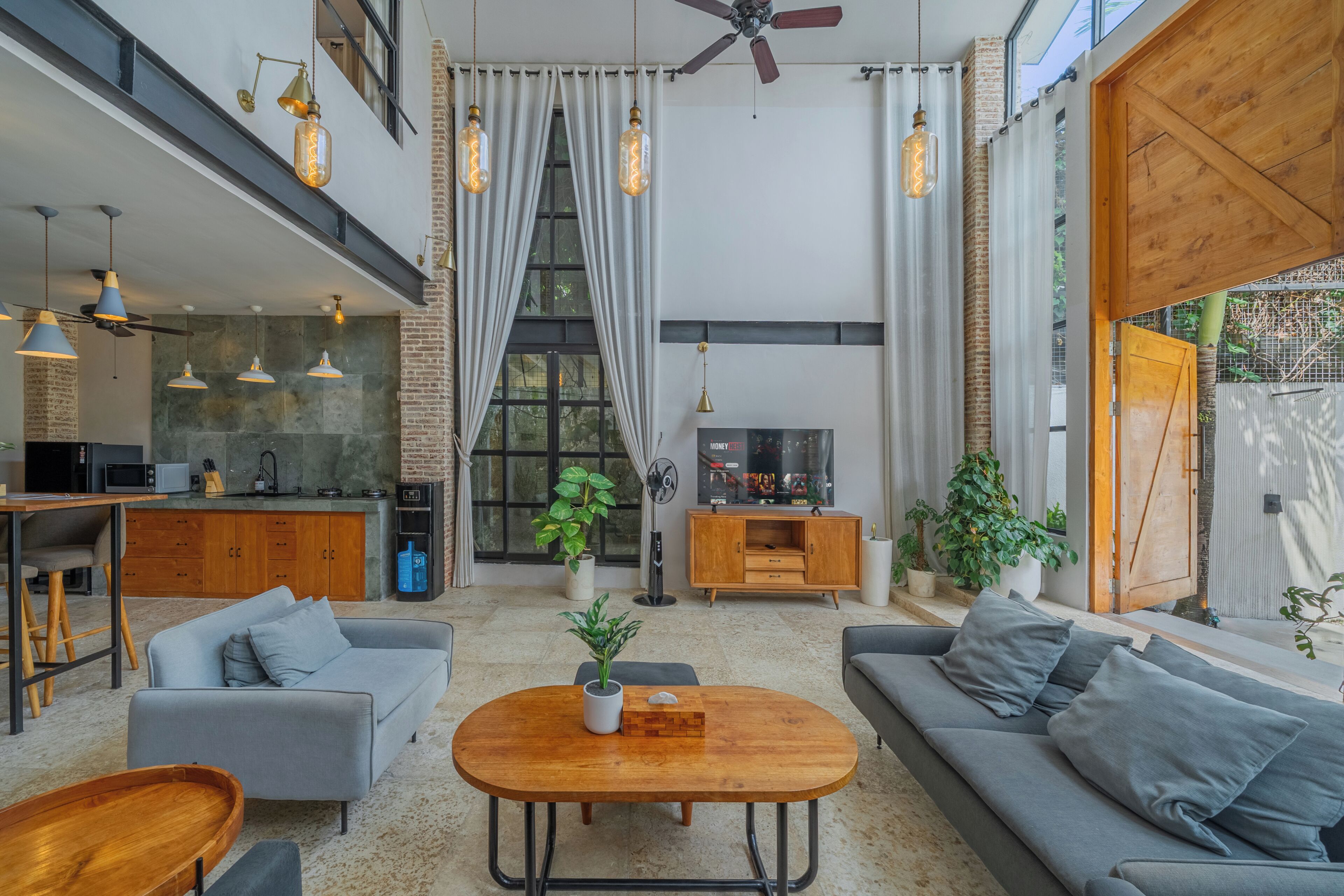 A spacious living area with a high ceiling, a built-in kitchen, and a large window.