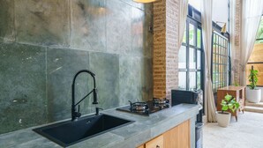 A modern kitchen with a large sink, gas stove, and a brick wall. - Villa Upeksha (Canggu)
