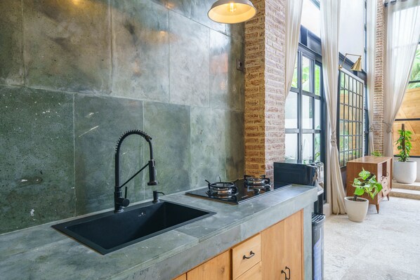 A modern kitchen with a large sink, gas stove, and a brick wall.