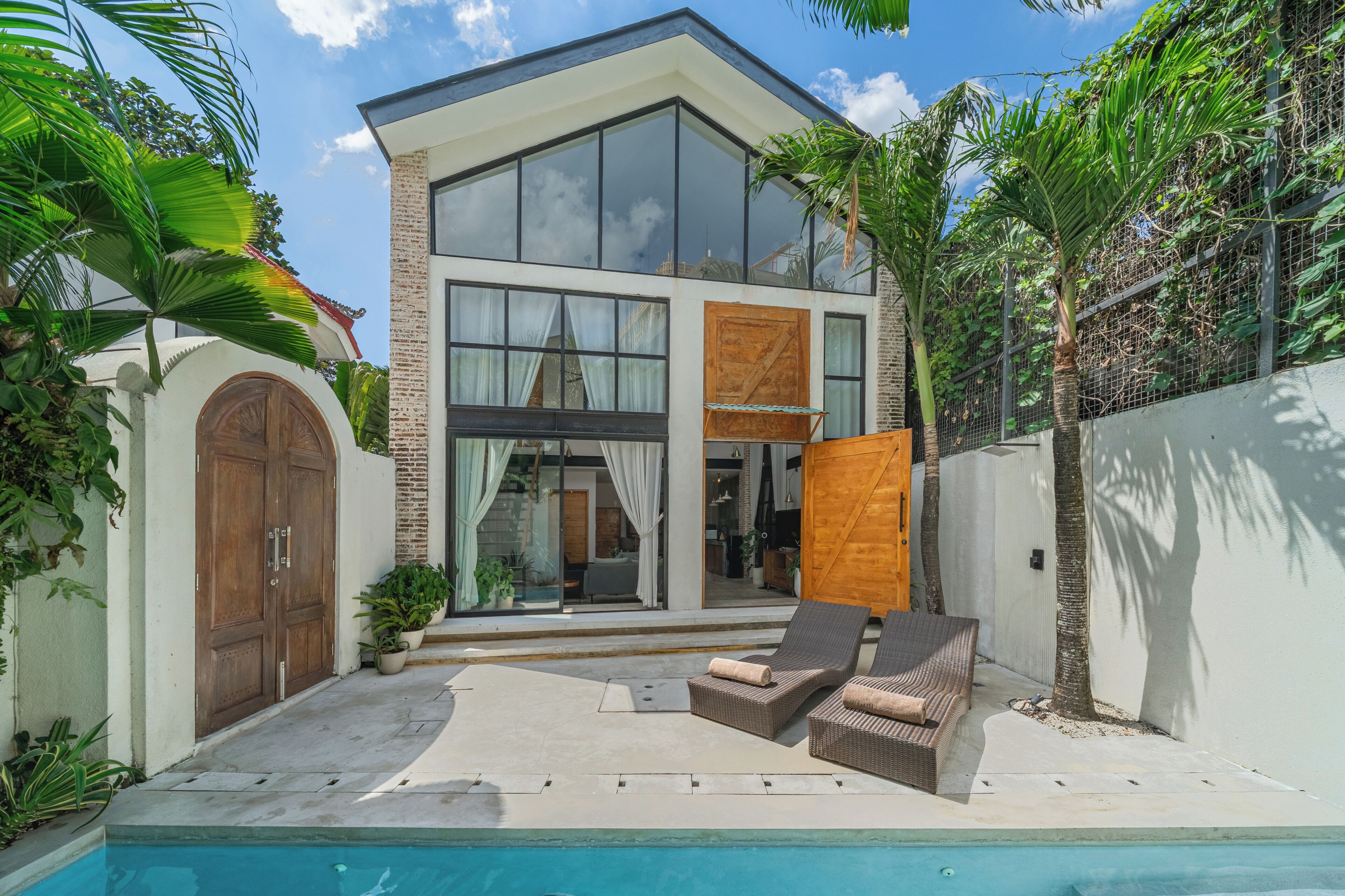 Una casa moderna de dos pisos con piscina, mobiliario exterior y abundante vegetación.