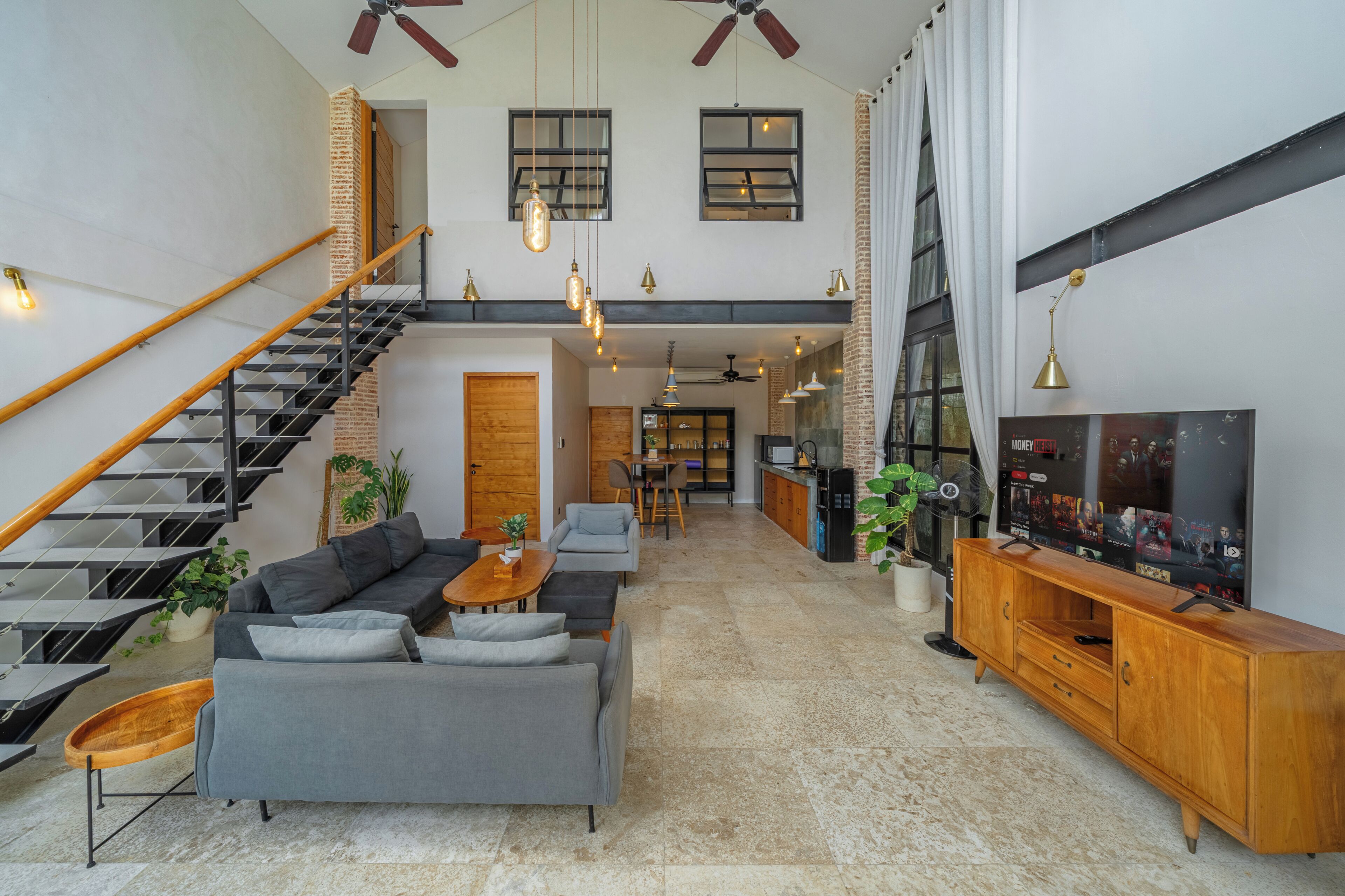 A spacious living area with a staircase, a sofa set, a wooden entertainment unit, and a television.